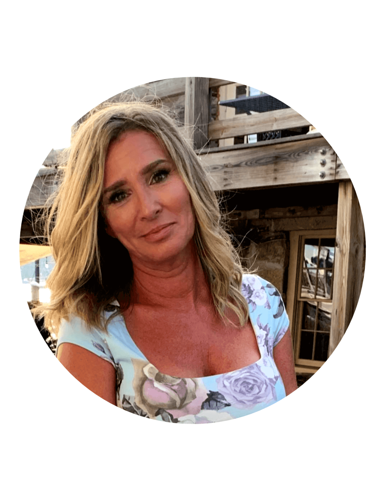 A woman smiling outdoors with a rustic wooden background.