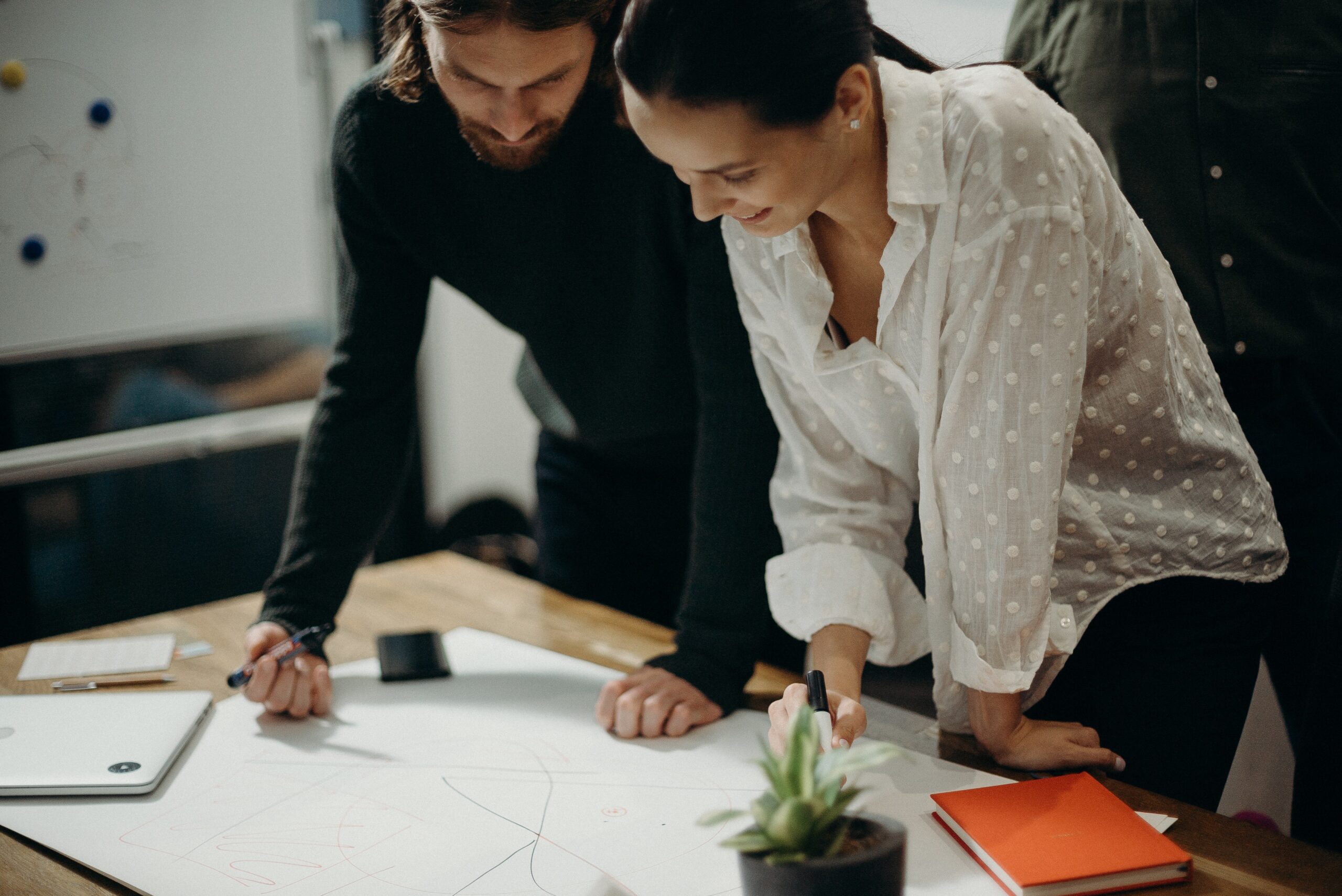 Two people collaborating over a blueprint at a table indoors.