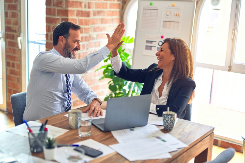 Two colleagues sharing a high-five in a lively office setting.