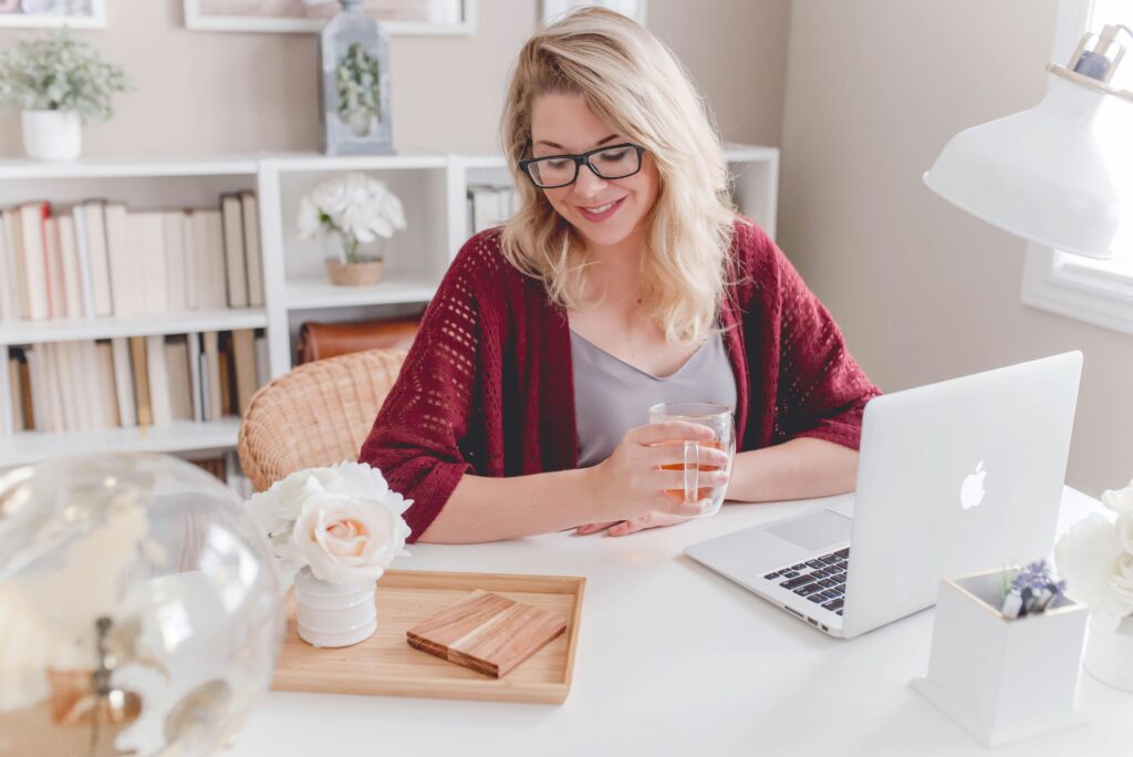 Woman with glasses working at a laptop and drinking coffee.
