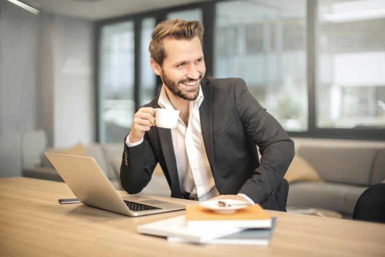 Smiling businessman holding a cup at his desk.