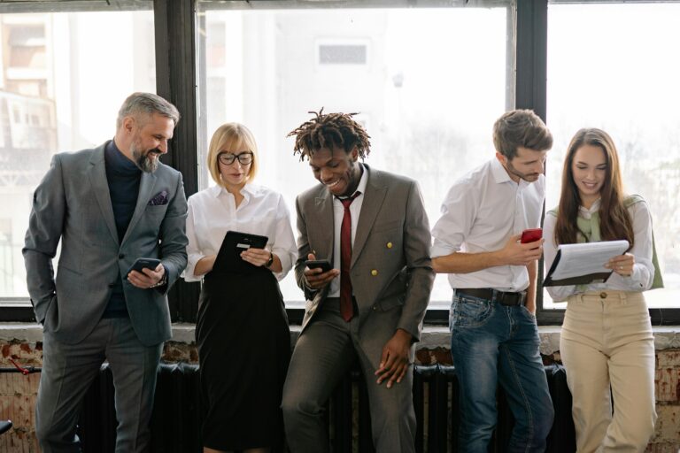 Four colleagues in business attire chatting and using smartphones by a window.