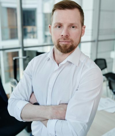Man in a white shirt standing confidently with arms crossed in an office.